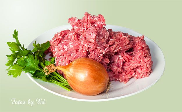 Frisches, rohes Hackfleisch mit Zwiebel und Petersilie auf einem Teller präsentiert.